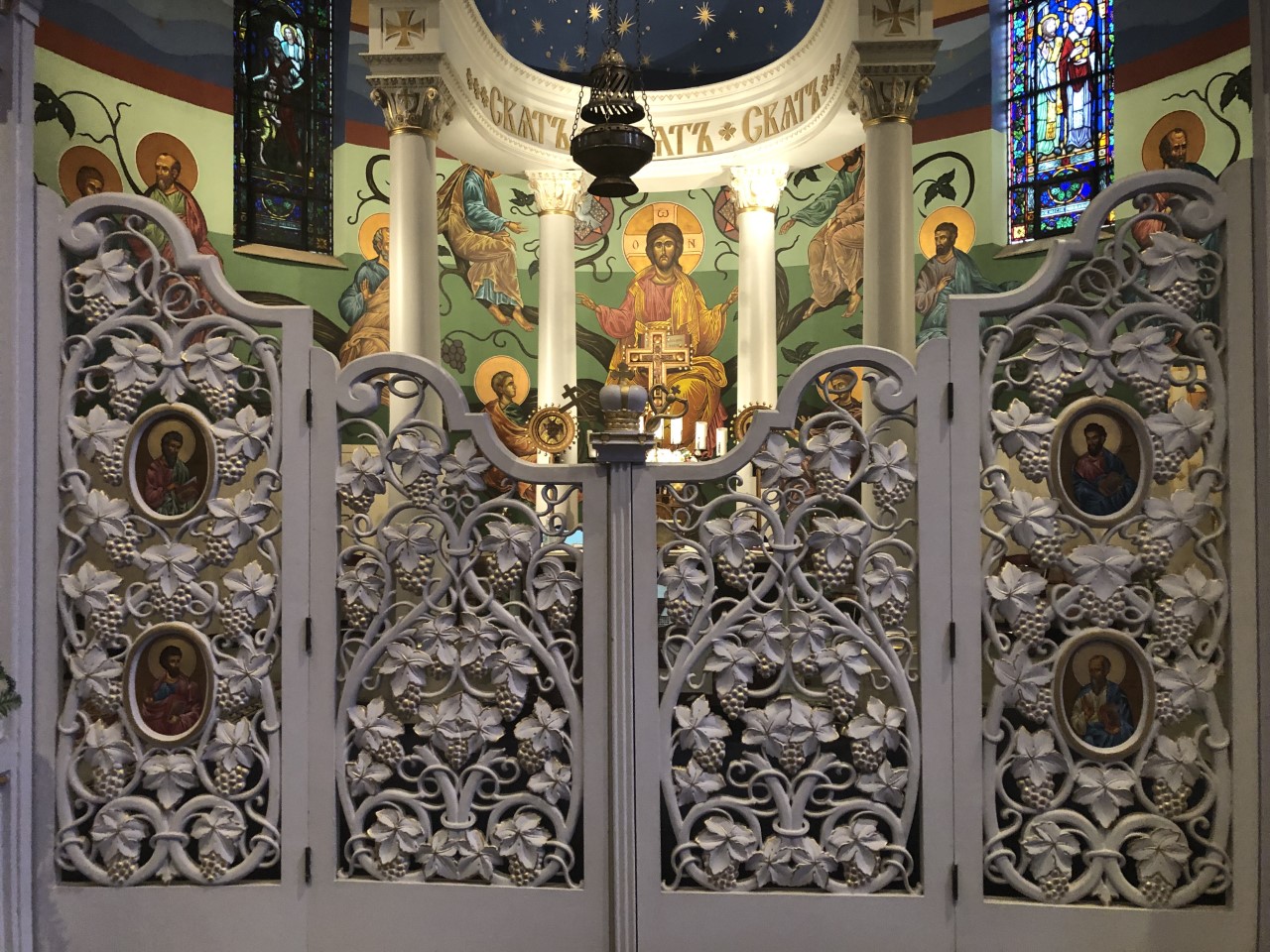 A four-part, gray, intricate gate with four portraits of gospel writers on the left and right parts of the gate. Behind it there is an image of Jesus in the center. 