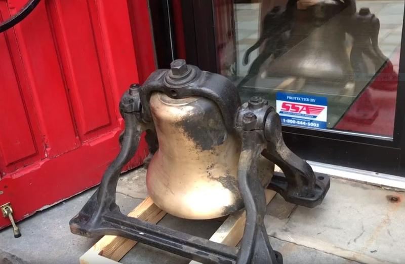 Large, old bell sitting on the ground beside a red door