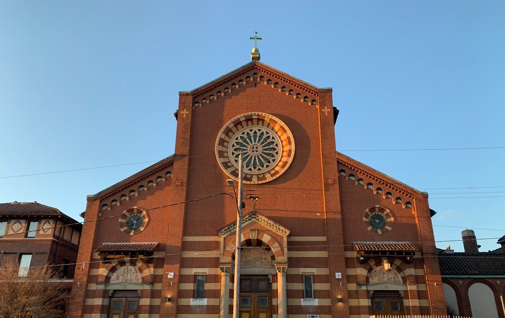 large brick building with circular window in center and cross at the top