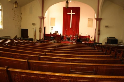 many rows of pews in front of a stage with a cross on the wall