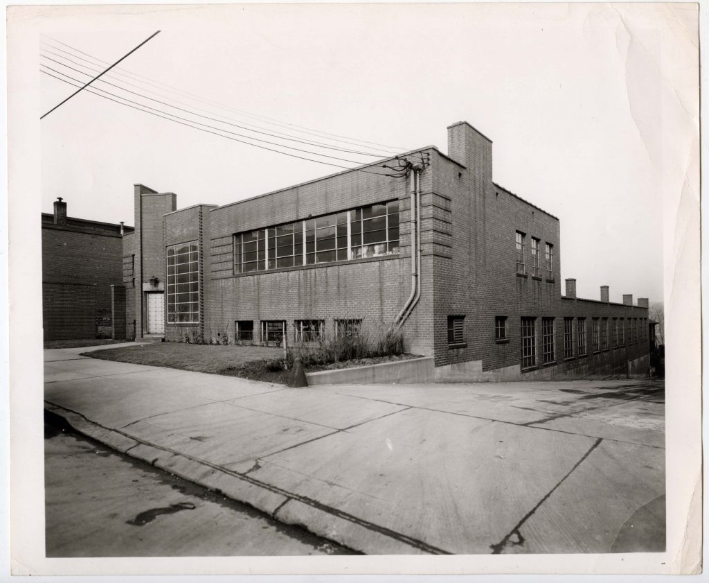 black and white photo of brick building with few windows and small parking lot
